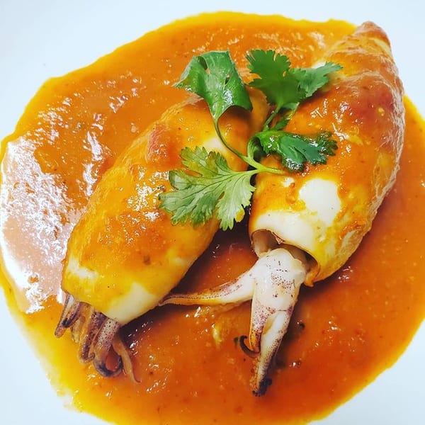 Two stuffed squid in a vibrant orange sauce, garnished with fresh cilantro on a white plate.