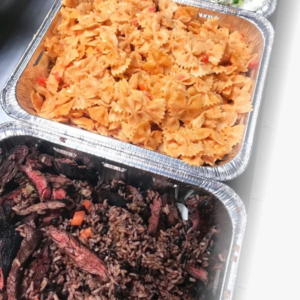 Two foil trays of food: creamy bow-tie pasta with red peppers, and rice with black beans and sliced steak.