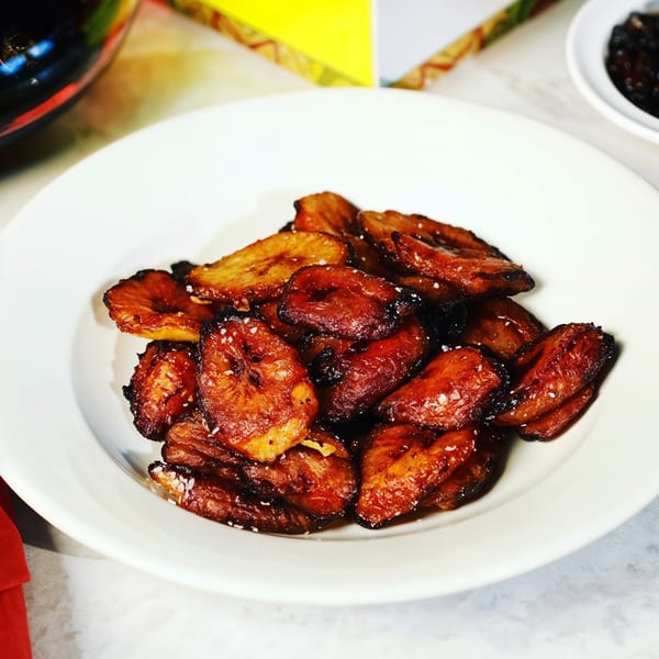 A white bowl filled with golden-brown, caramelized sweet plantains, sprinkled with sea salt.