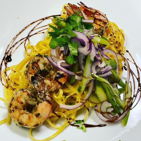 Lola Latin Bistro's grilled shrimp pasta with red onions, green vegetables, and a balsamic drizzle.